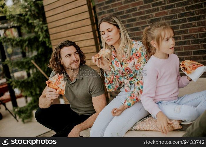 Happy young family eating pizza in the house backyard