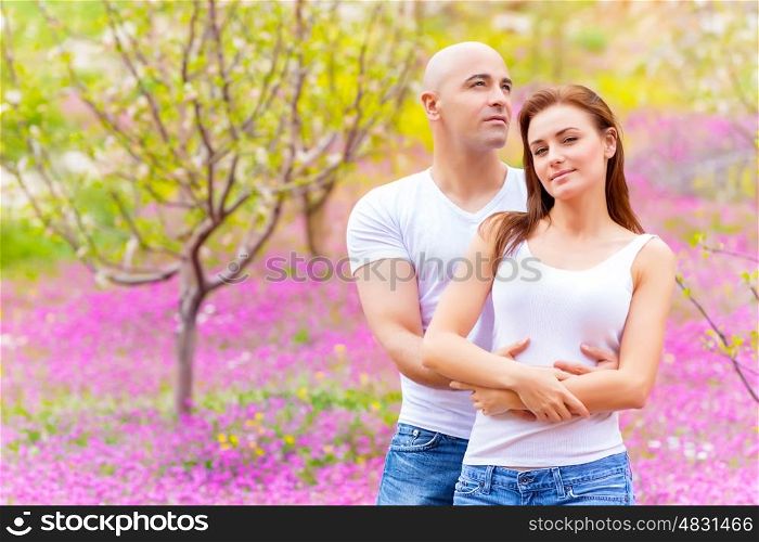 Happy young family embracing on purple floral field, having fun outdoors, first love, spring nature, affection concept