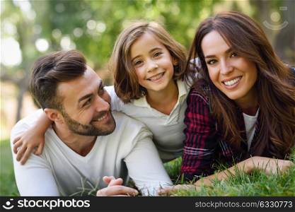 Happy young family in a urban park. Father, mother and little daughter laying on grass.