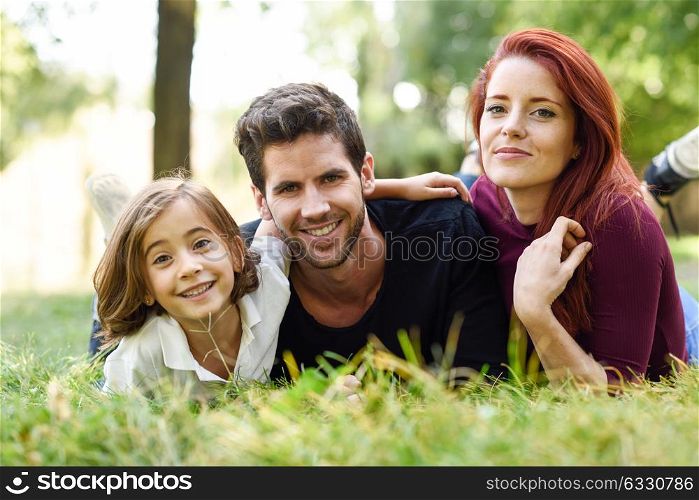 Happy young family in a urban park. Father, mother and little daughter laying on grass.