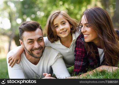 Happy young family in a urban park. Father, mother and little daughter laying on grass.. Happy young family in a urban park