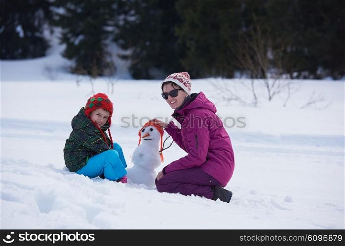 happy young family playing in fresh snow and building snowman at beautiful sunny winter day outdoor in nature