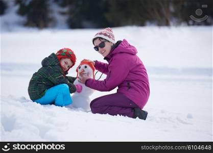 happy young family playing in fresh snow and building snowman at beautiful sunny winter day outdoor in nature