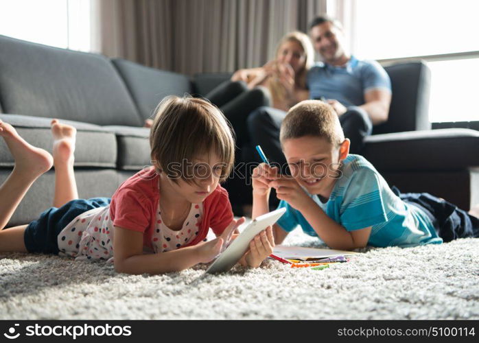 Happy Young Family Playing Together at home on the floor using a tablet and a children&rsquo;s drawing set