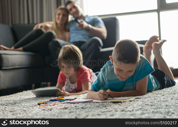 Happy Young Family Playing Together at home on the floor using a tablet and a children&rsquo;s drawing set