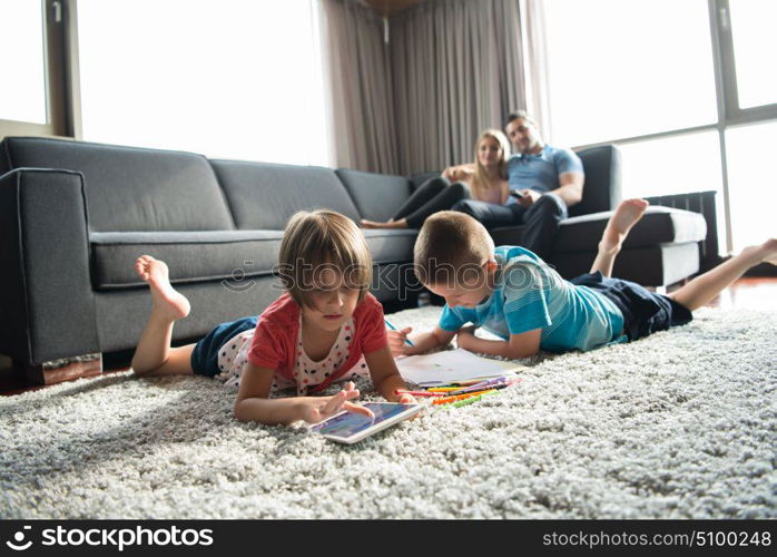 Happy Young Family Playing Together at home on the floor using a tablet and a children&rsquo;s drawing set