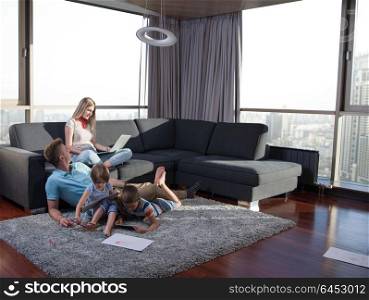 Happy Young Family Playing Together at home on the floor using a laptop computer and a children&rsquo;s drawing set