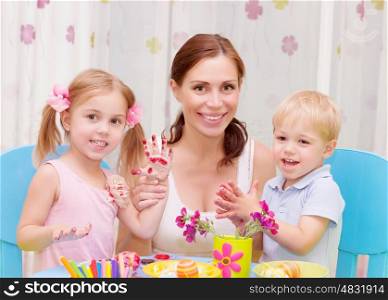 Happy young family playing with colorful paint at home, mother with two adorable children decorate Easter eggs