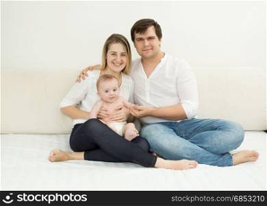 Happy young family posing with baby son on bed