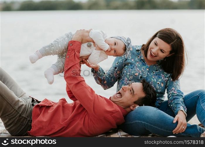 Happy young family sitting near the water. Mom, dad and their little baby daughter sitting together. Happy family outdoors. Smiling people. Happy young family sitting near the water. Mom, dad and their little baby daughter sitting together. Happy family outdoors. Smiling people.