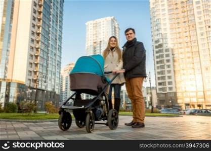 Happy young family walking with pram on street at sunny day