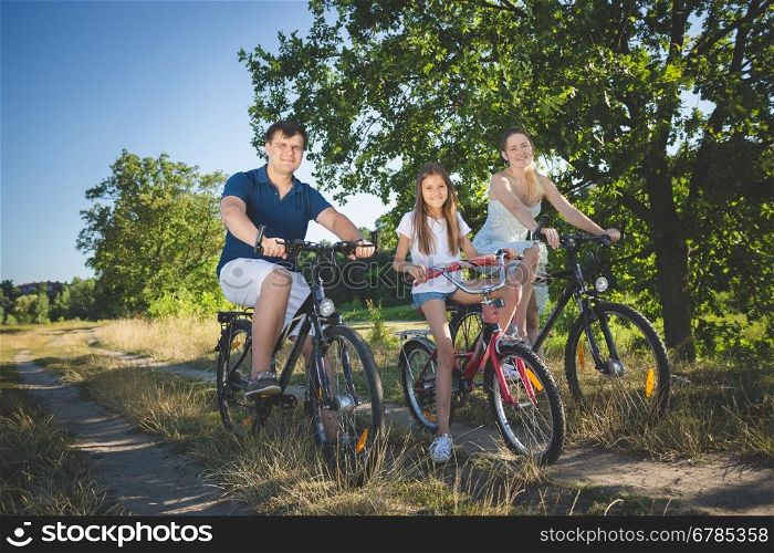 Happy young family with cute daughter cycling at meadow