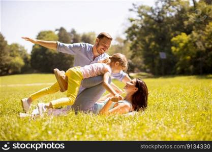 Happy young family with cute little daughter having fun in park on a sunny day