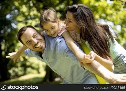 Happy young family with cute little daughter having fun in park on a sunny day