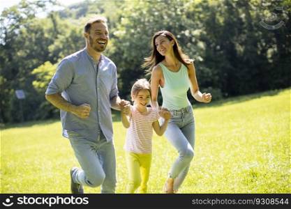 Happy young family with cute little daughter running in park on a sunny day