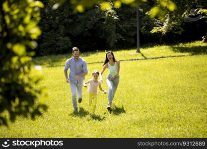 Happy young family with cute little daughter running in park on a sunny day