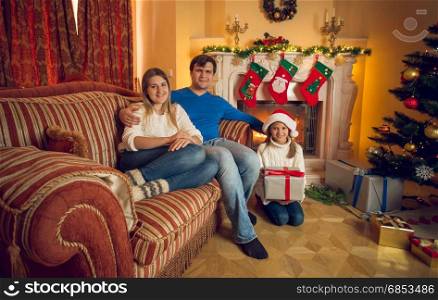 Happy young family with daughter posing at living room with fireplace