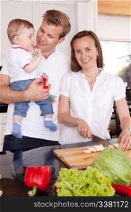 Happy young family with mother father and young toddler son in the kitchen preparing food