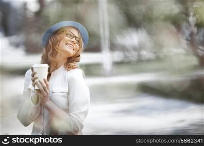 Happy young fashionable woman taking a coffee break after shopping, smiling with a coffee-to-go in her hands in a summer park.