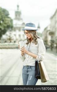 Happy young fashionable woman with shopping bags enjoying drinking coffee after shopping and holding take away coffee against urban background.
