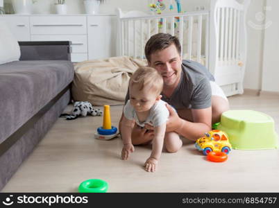 Happy young father crawling with his baby boy on floor at living room