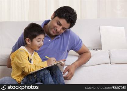 Happy young father helping his son in drawing at home