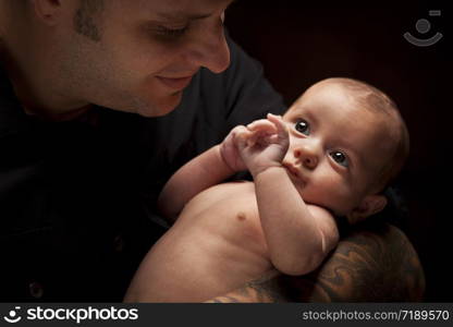 Happy Young Father Holding His Mixed Race Newborn Baby Under Dramatic Lighting.