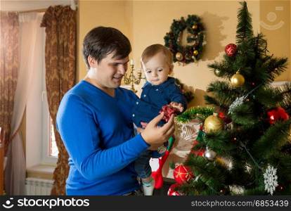 Happy young father hugging his 1 year old baby son near Christmas tree