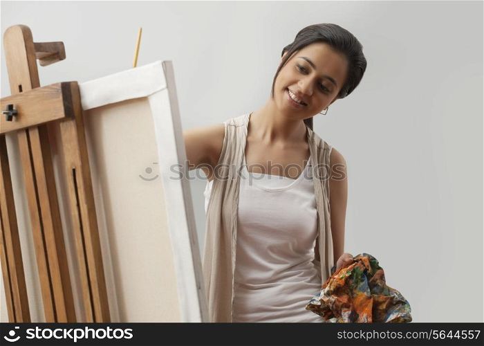 Happy young female artist painting on canvas isolated over gray background
