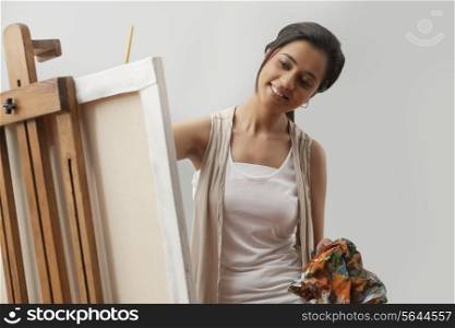 Happy young female artist painting on canvas isolated over gray background