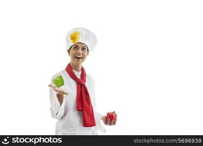 Happy young female chef juggling bell peppers isolated over white background
