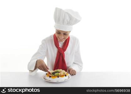 Happy young female chef making mixed fruit cake isolated over white background
