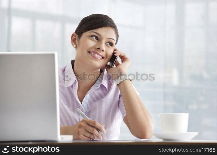 Happy young female executive using cell phone at her desk