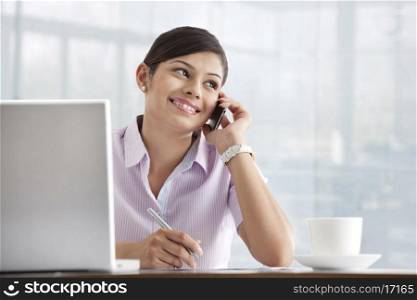 Happy young female executive using cell phone at her desk