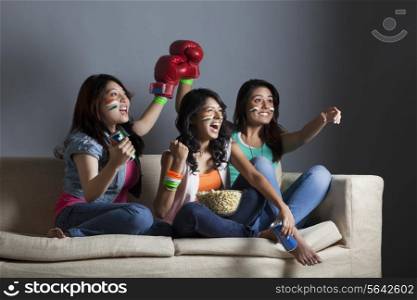 Happy young female friends watching boxing match together at home