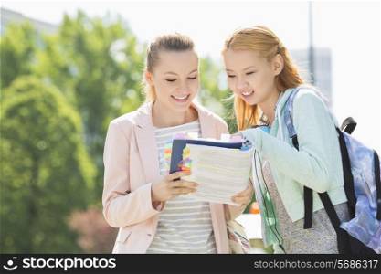Happy young female students reading book at college campus