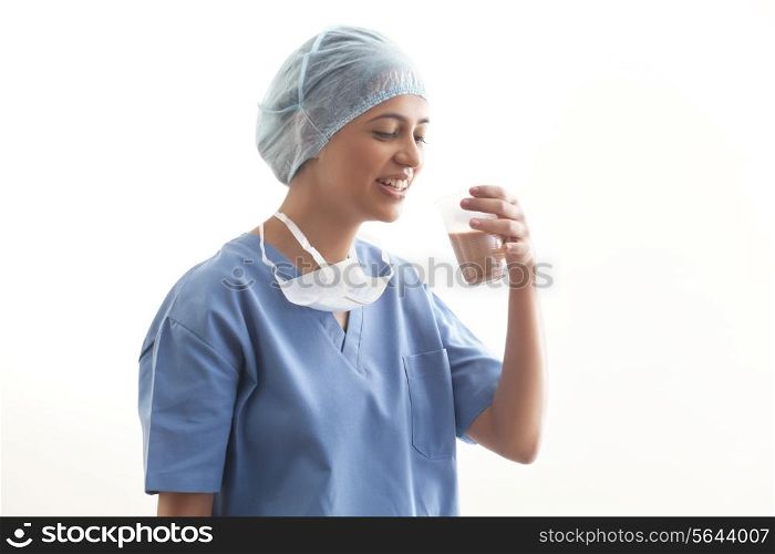 Happy young female surgeon drinking tea isolated over white background