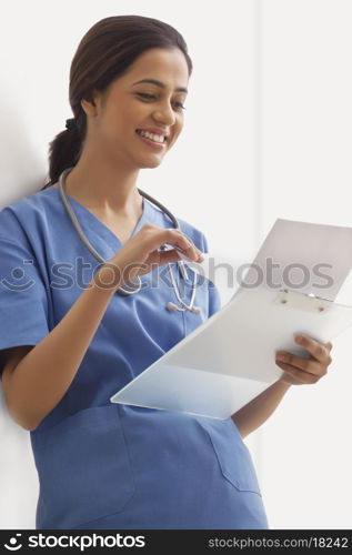 Happy young female surgeon reading notes on clip board