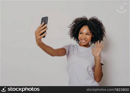 Happy young female waving at camera while having video call with best friend on modern smartphone, young cheerful african woman expressing positiveness while talking with followers in social media. Happy young female waving at camera while having video call with best friend on modern smartphone