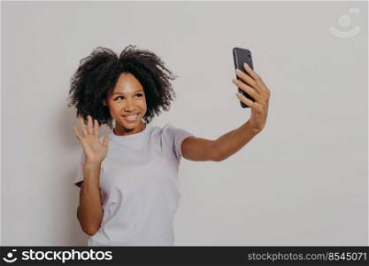 Happy young female waving at camera while having video call with best friend on modern smartphone, young cheerful african woman expressing positiveness while talking with followers in social media. Happy young female waving at camera while having video call with best friend on modern smartphone