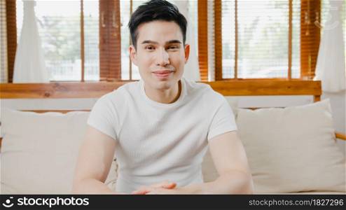 Happy young freelance asia man looking at camera smiling and cheerful relax on video call online on sofa in living room at home, Stay at house quarantine, work from home, Social distancing concept.