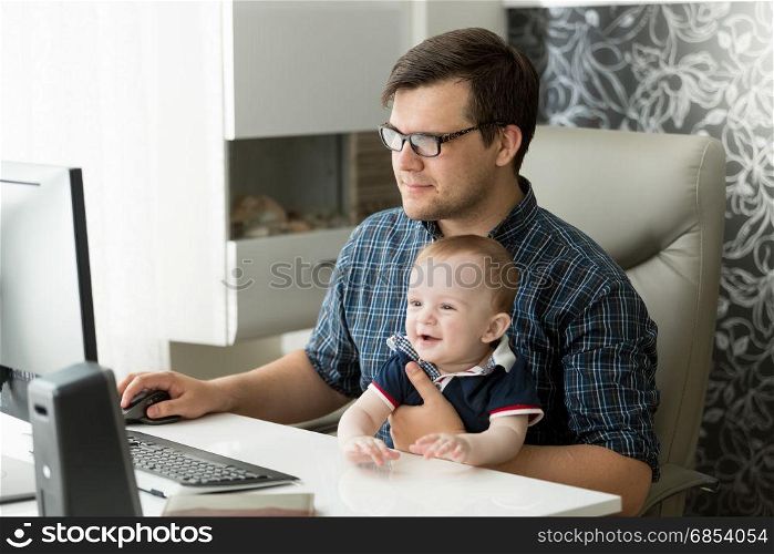 Happy young freelancer businessman working at home and taking care of his baby
