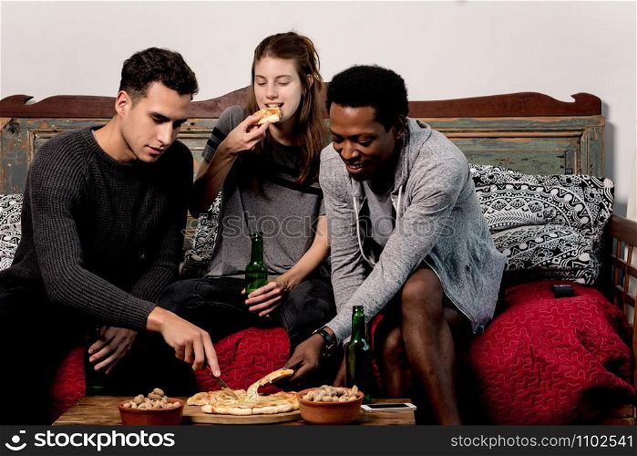 happy young friends eating pizza with beer on sofa at home.