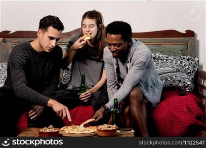 happy young friends eating pizza with beer on sofa at home.