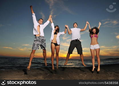 happy young friends group have fun and celebrate while jumping and running on the beach at the sunset