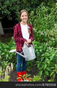 Happy young girl in red rubber boots watering vegetables at garden