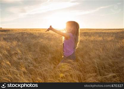 happy young girl joys at the wheat field at the evening time
