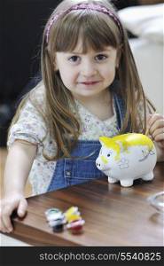 happy young girl portrait at home while painting piggy bank and representing banking and finance concept