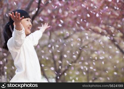 Happy young girl throwing cherry blossom petals in the air outside in a park in springtime