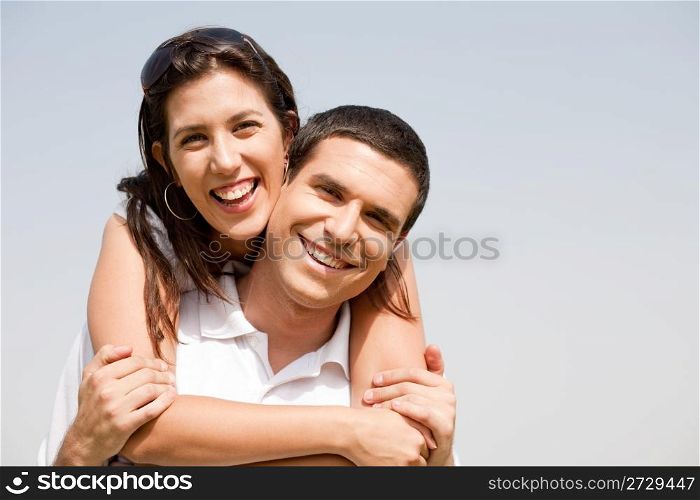 Happy young guy piggybacking his girlfriend under the sky view